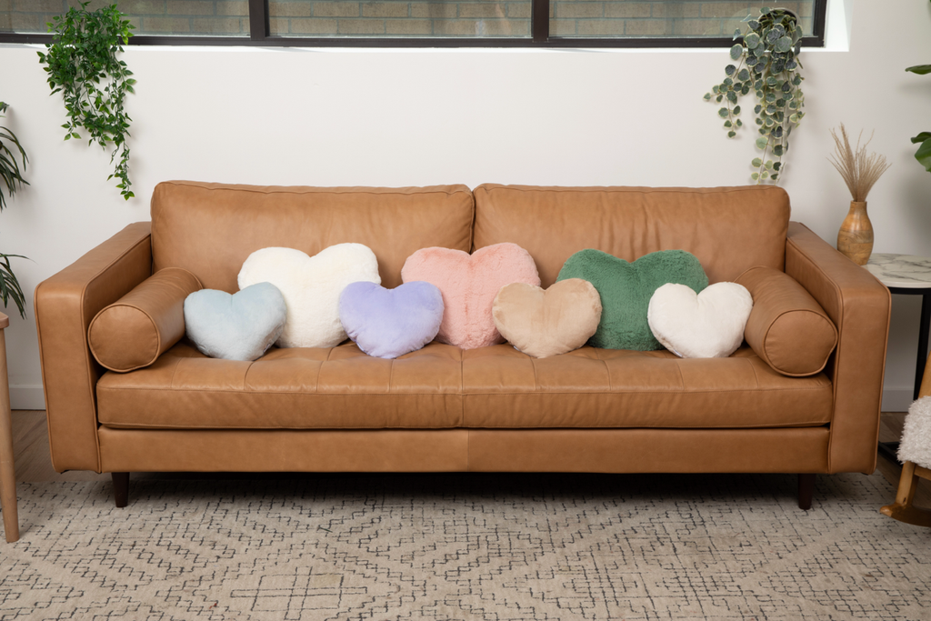 Image shows various colors and sizes of heart-shaped weighted pillows on couch