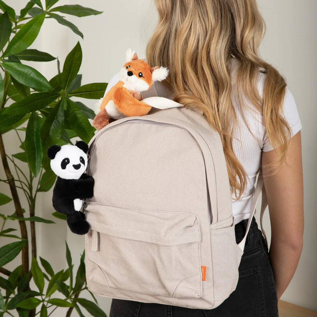 Person with a beige backpack featuring a stuffed hugimal baby fox and hugimal baby panda, standing indoors next to a plant.